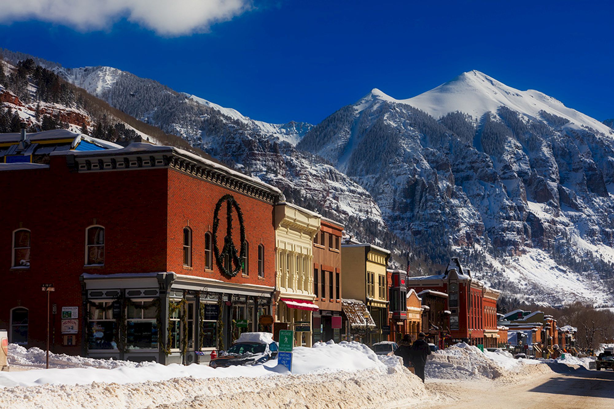 A snowy mountain town with colorful buildings, a large peace sign on one, under a clear blue sky and bright sunlight.