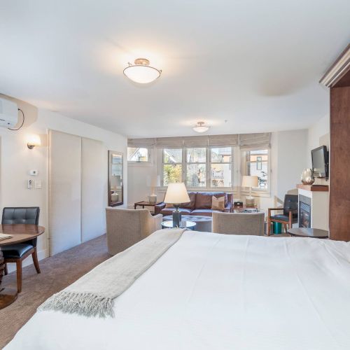 A neat and well-lit Hotel Columbia Telluride room with a bed, artwork, seating area, and a desk.