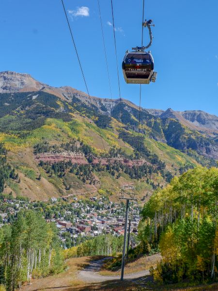 A gondola soars above a scenic mountain town amidst autumn foliage in Telluride Colorado.