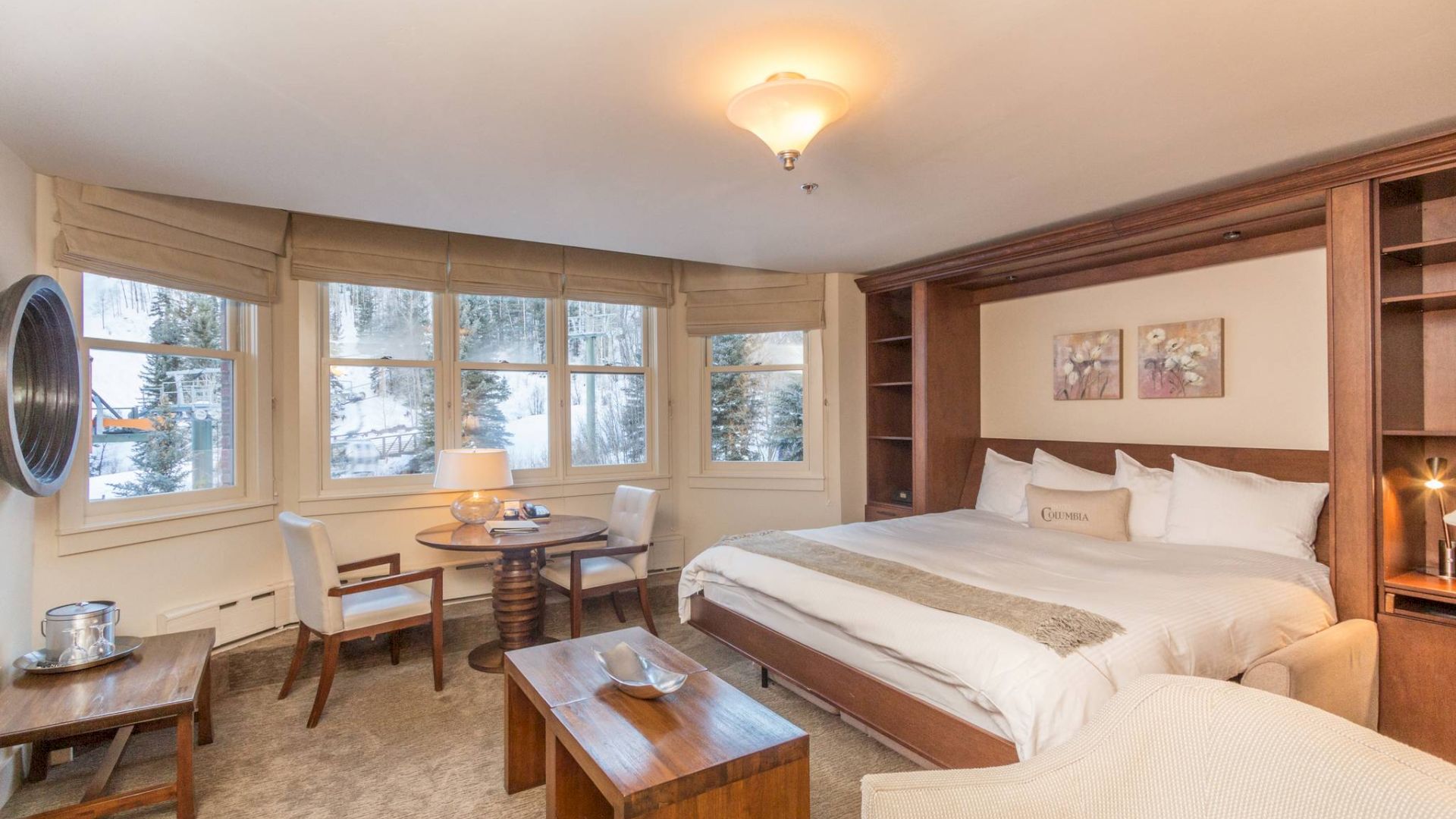 Cozy bedroom with a large bed, tables, chairs, and a ceiling light fixture.