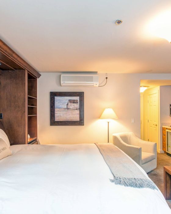 A cozy Hotel Columbia Telluride room with a bed, paintings, and a kitchenette in the back.