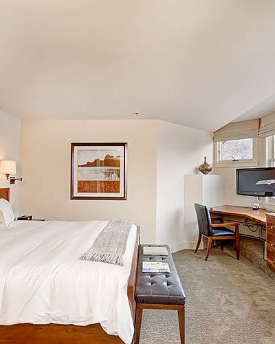 A cozy Hotel Columbia Telluride room with a bed, desk, TV, and window showing snow outside.