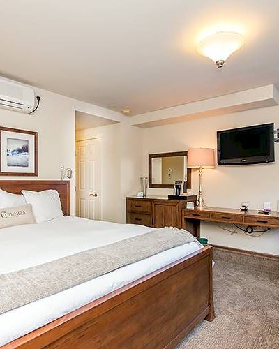 A Hotel Columbia Telluridel room with a large bed, TV, desk, chairs, and pictures on the wall.