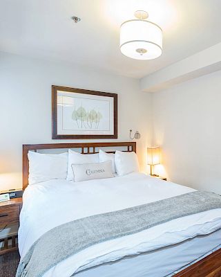 A tidy Hotel Columbia Telluride bedroom with a large bed, artwork, lamps, and a mirror on the wall.