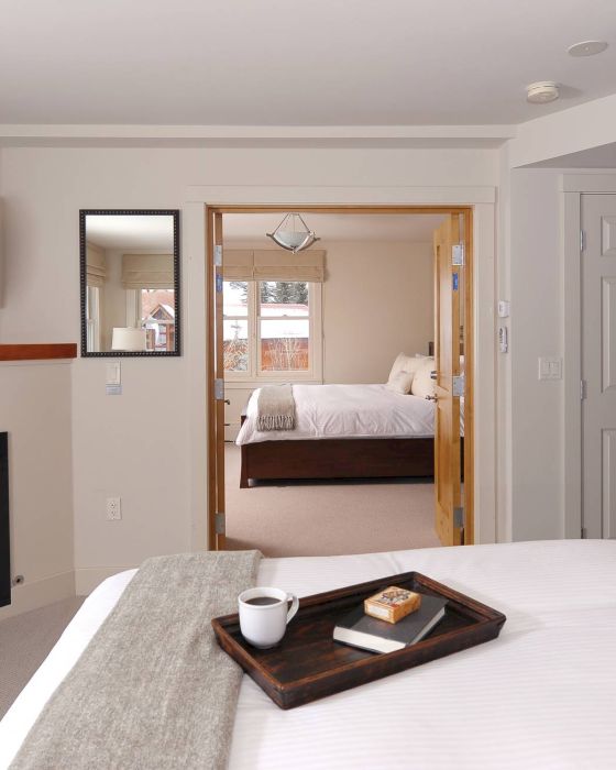 Cozy Hotel Columbia Telluride bedroom with a fireplace, TV, tray with food on the bed, and a view into another room.