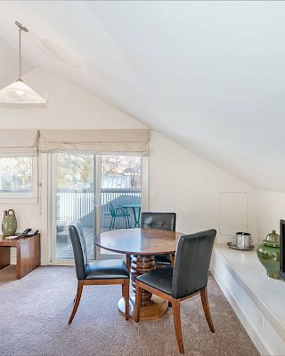 Bright, cozy attic room with dining table, chairs, TV, and sloped ceiling.