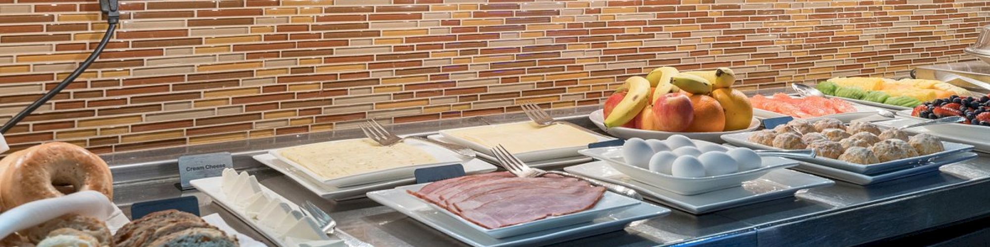 A buffet lineup at Hotel Columbia Telluride with fruits, meats, and bread under a kitchen hood.