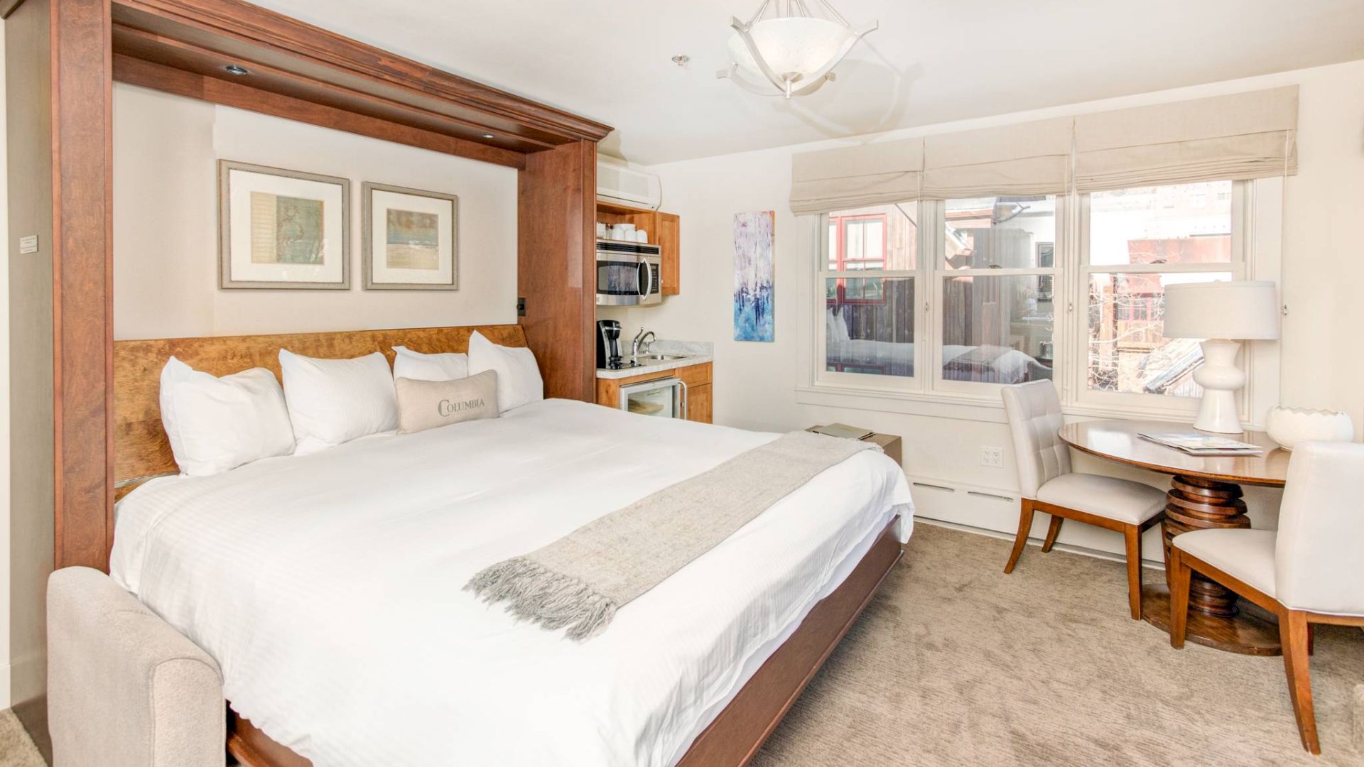 Bright Hotel Columbia Telluride room with a large bed, side tables, lamps, artwork, and a desk near the window.