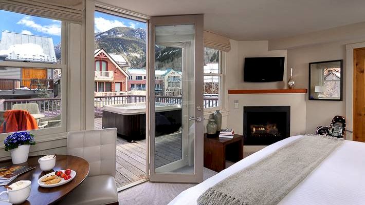 Hotel Columbia Telluride room with a bed, TV, fireplace, and a view of mountains through a balcony door.