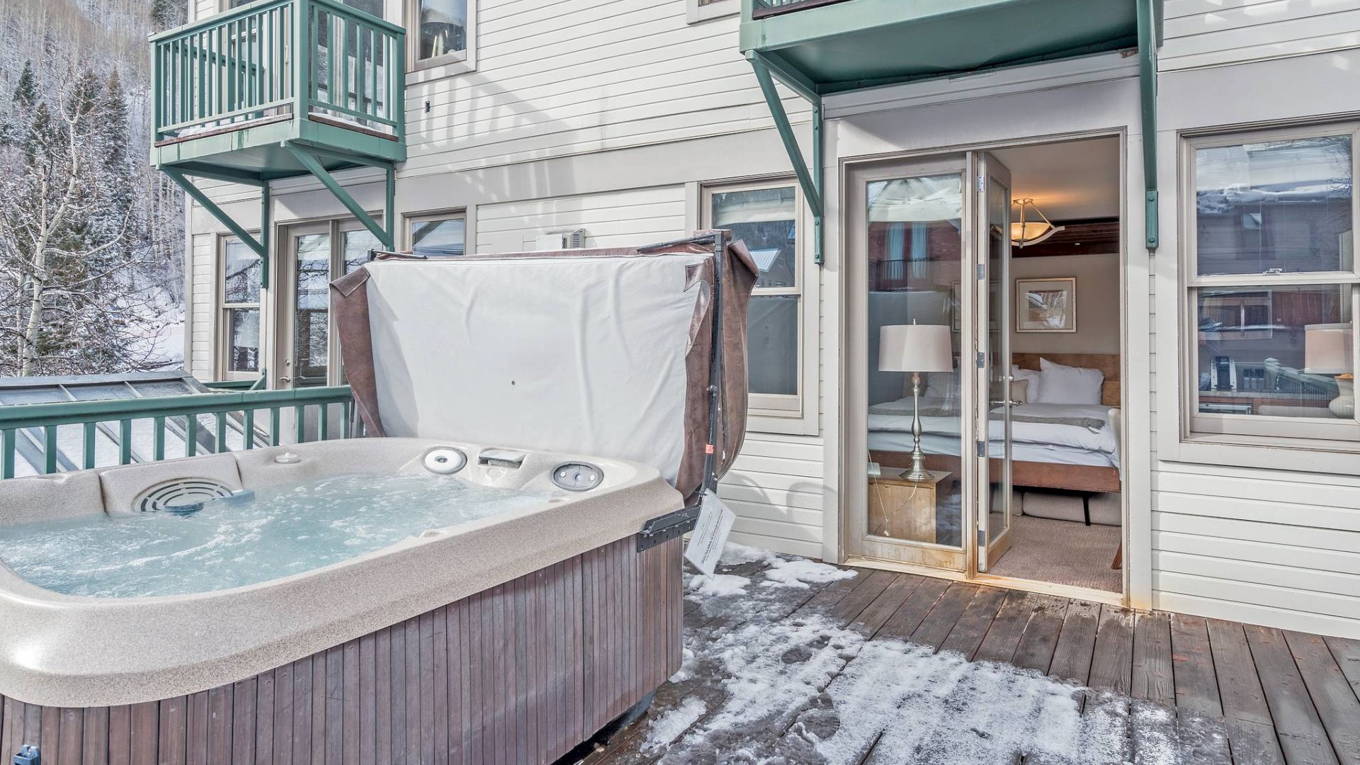 An outdoor hot tub on a snowy deck, next to a building with open doors.