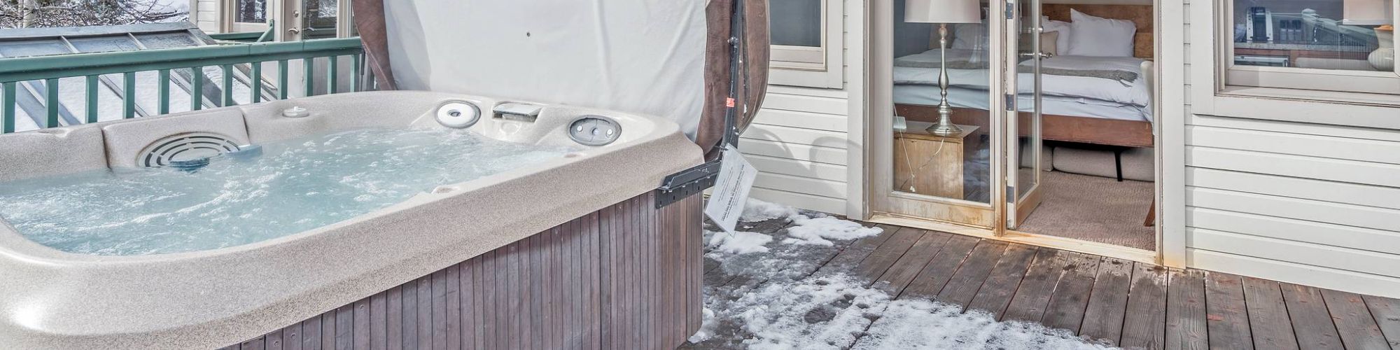 An outdoor hot tub on a snowy deck, next to a building with open doors.