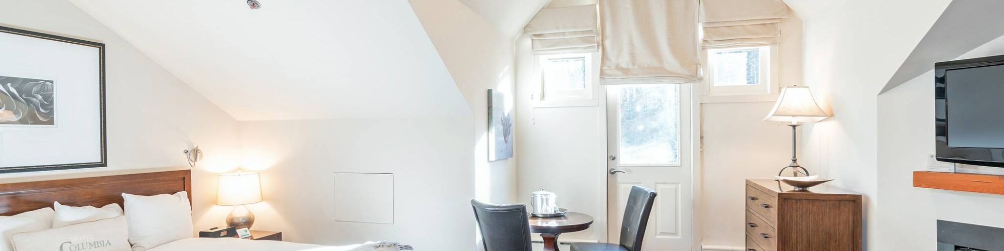 A cozy attic bedroom with a bed, fireplace, desk, chairs, and slanted ceilings.