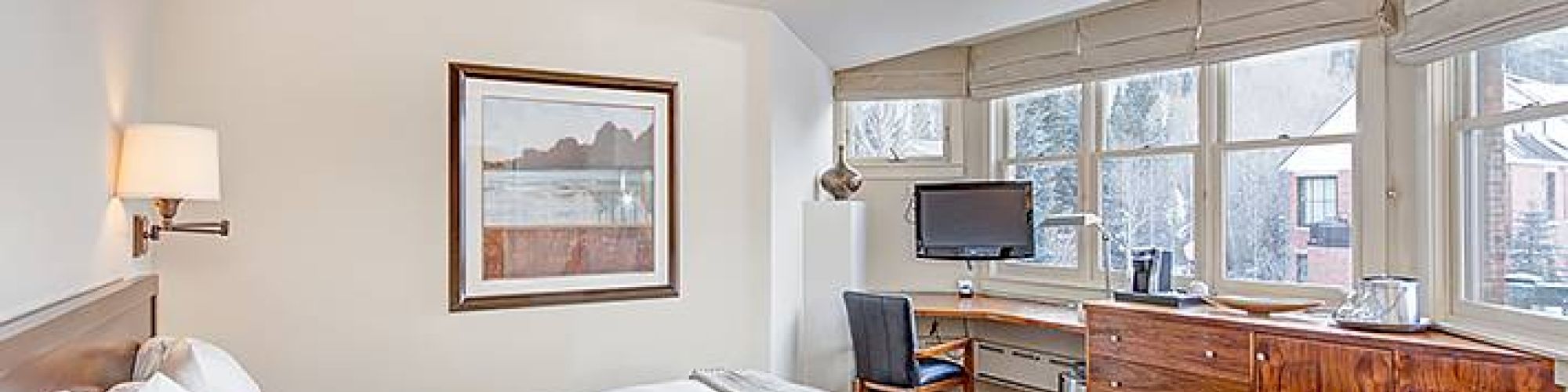 Bright, cozy room with a bed, desk, artwork, and snow view outside the window.