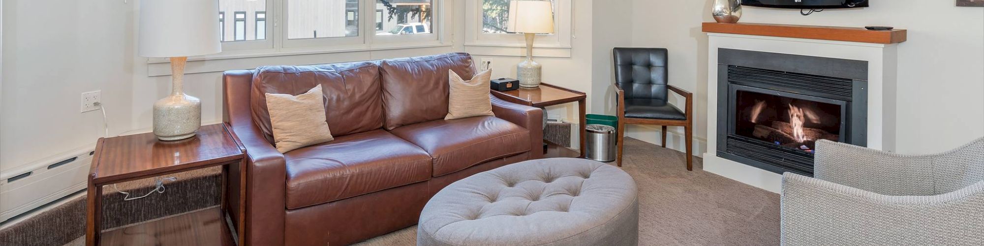 A cozy living room with a sofa, chairs, TV, fireplace, and windows.