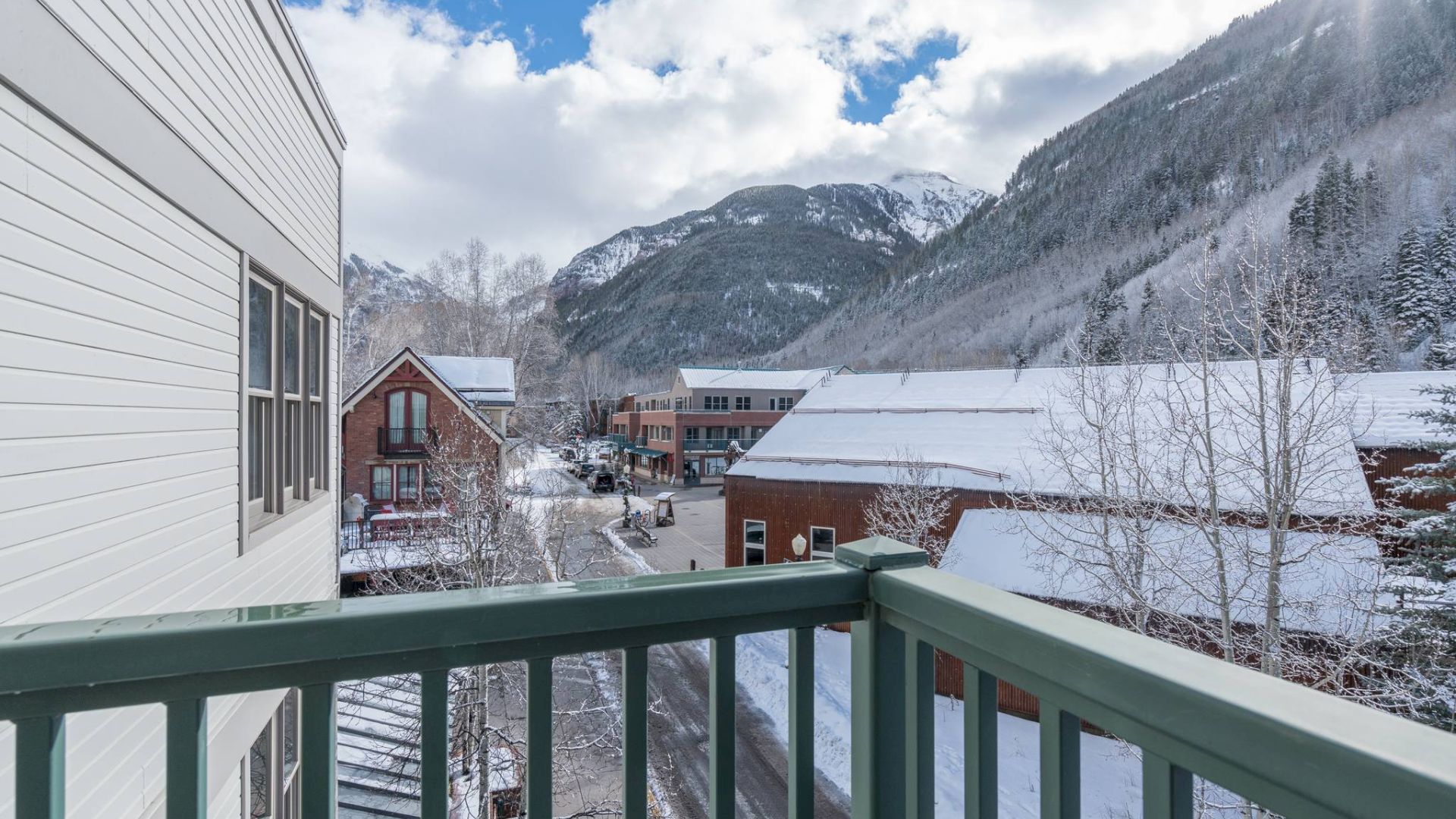 View from a balcony showing snow-covered mountains and buildings in a small town.