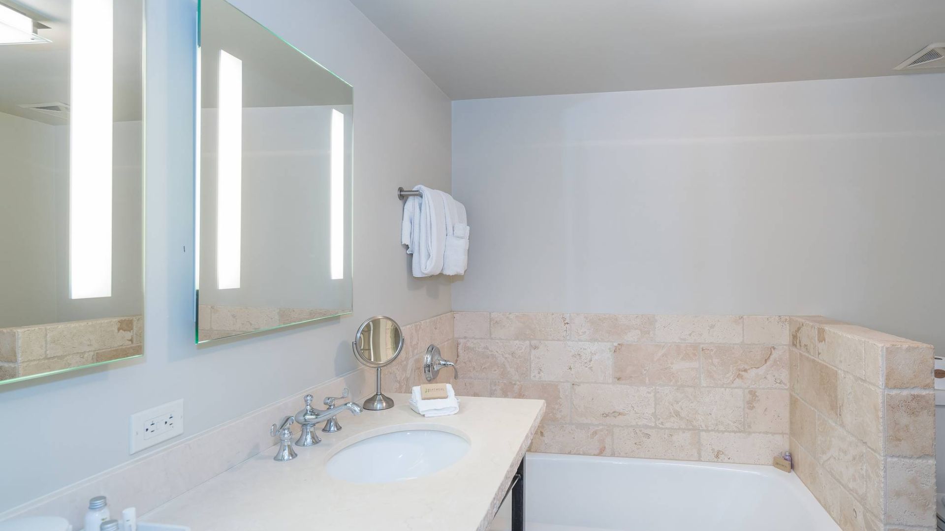 A clean, bright bathroom with a sink, mirror, bathtub, and toiletries.