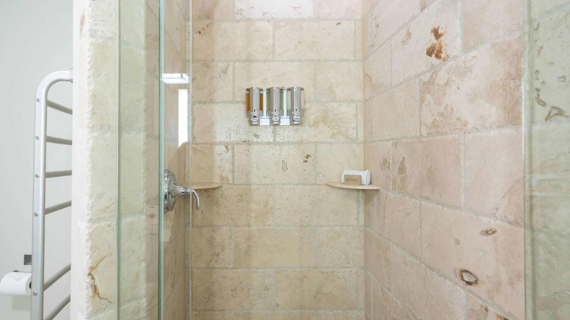 It's a shower with beige tiles, a glass door, and toiletries.