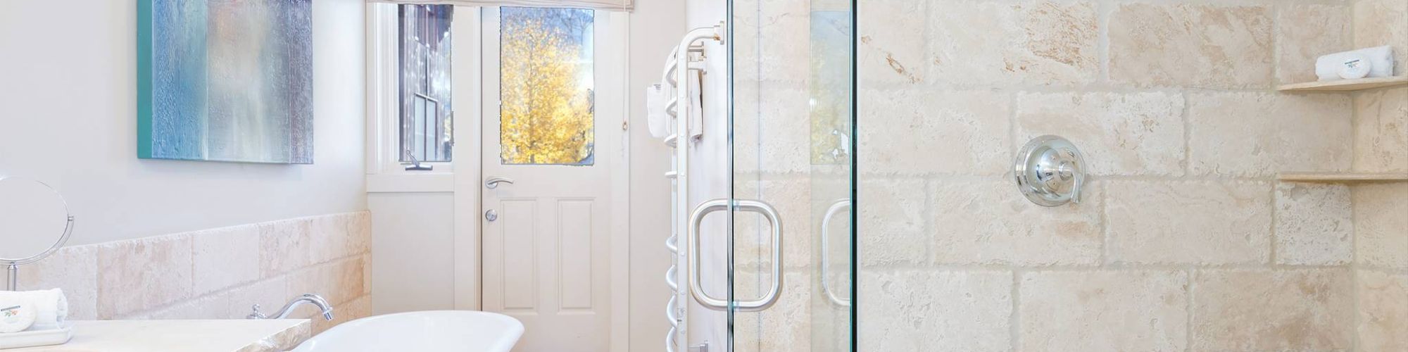 A bright bathroom with a tub, sink, glass shower, and a painting.