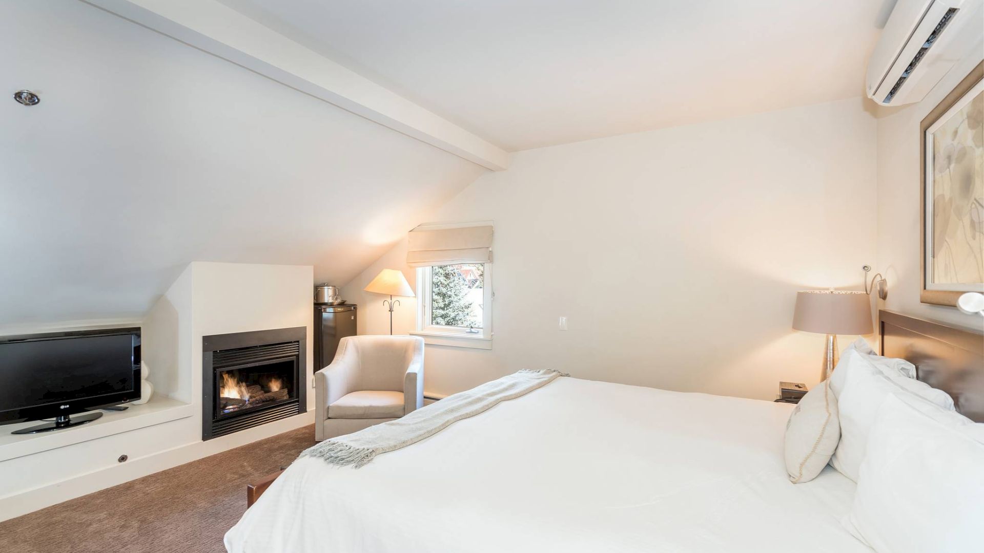 A cozy Hotel Columbia Telluride bedroom with a large bed, fireplace, TV, and slanted ceiling.