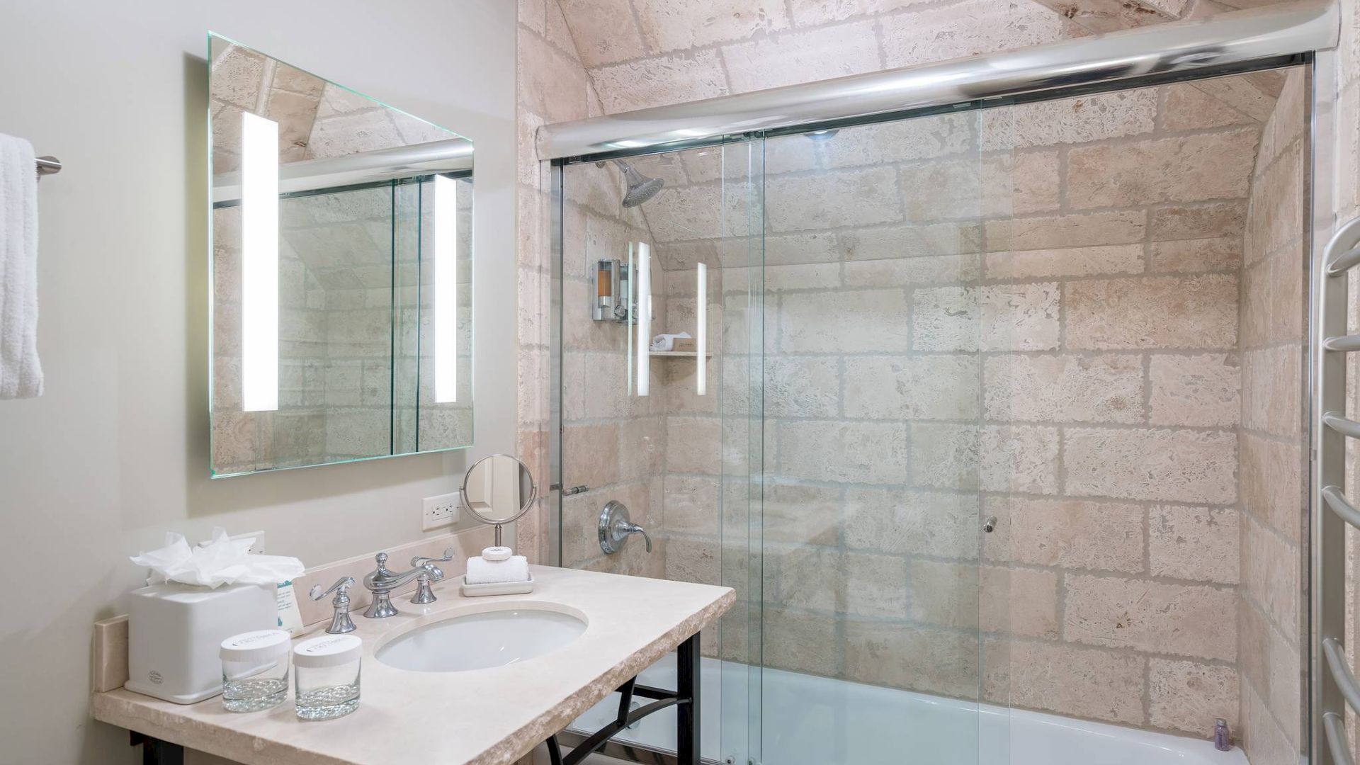 A modern bathroom with a glass shower, sink, mirror, and tiled walls.