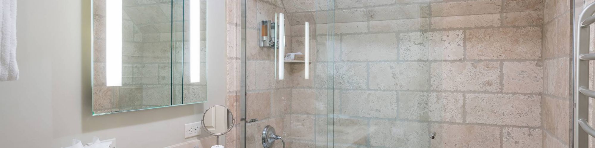 A modern bathroom with a glass shower, sink, mirror, and tiled walls.