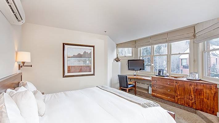 A tidy Hotel Columbia Telluride bedroom with a made bed, desk, chair, and a picture on the wall.