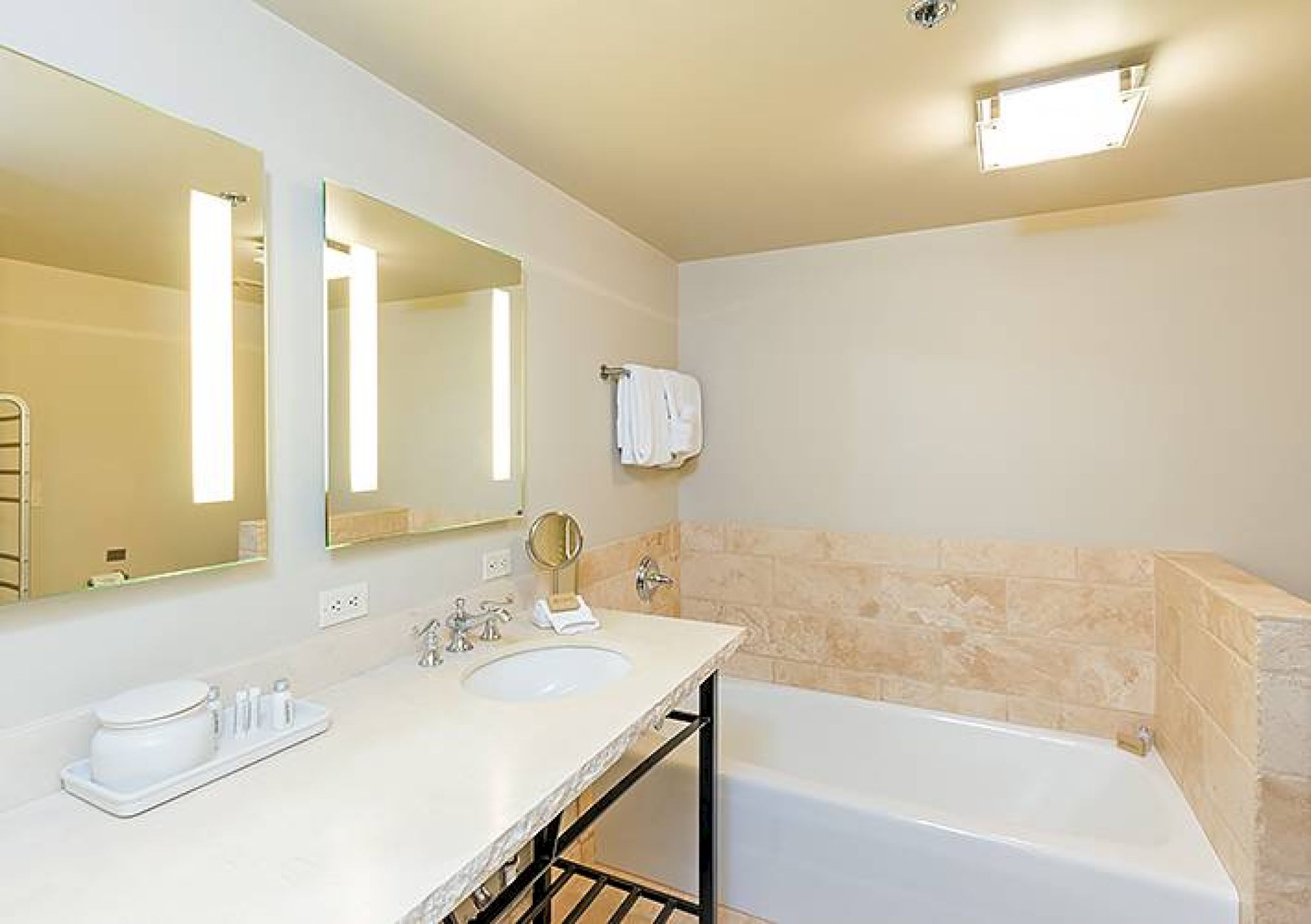 A clean, modern bathroom with a large mirror, sink, bathtub, and towels.