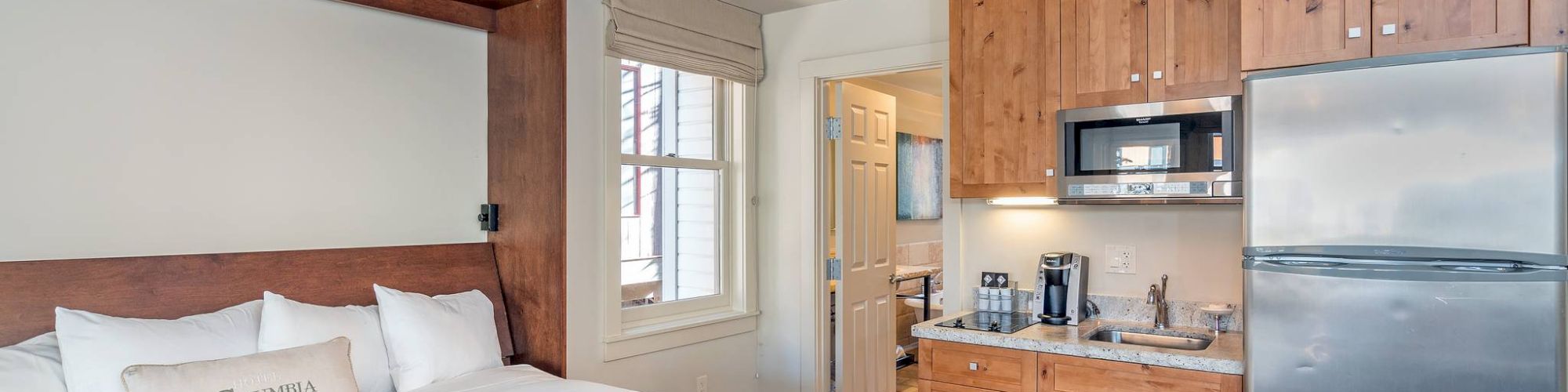 A Hotel Columbia Telluride room with a bed, kitchen appliances, and wooden cabinets.