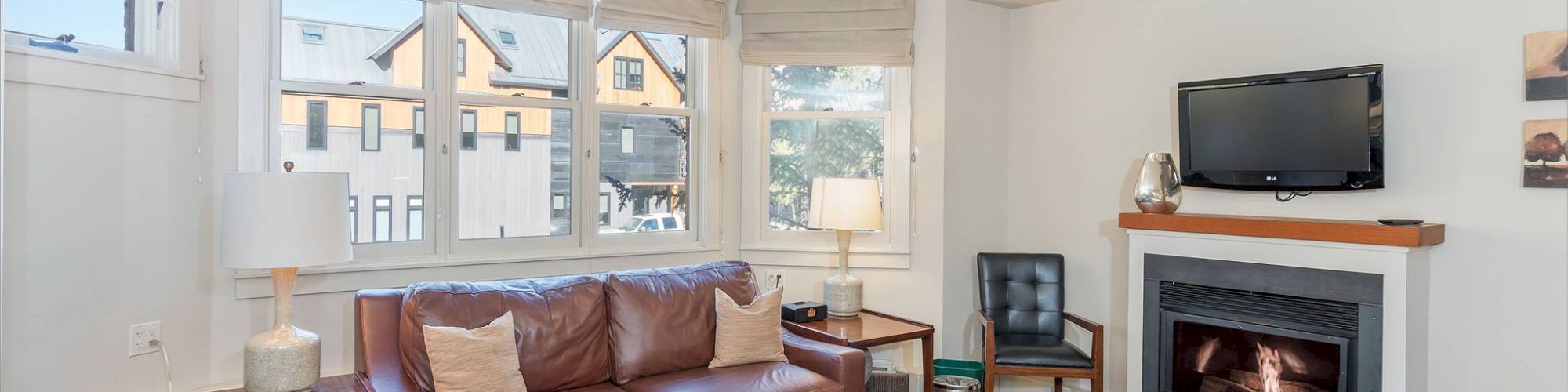 A cozy living room with a sofa, fireplace, TV, and windows with a view outside.