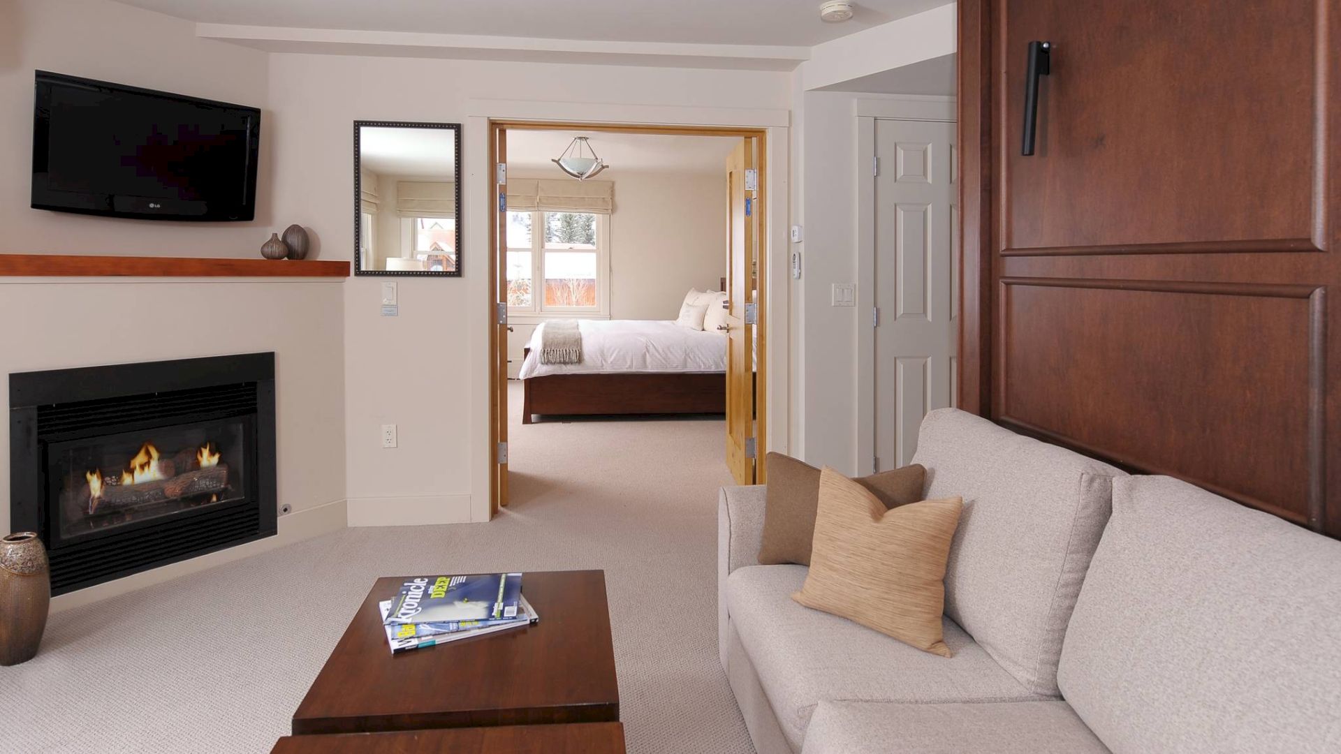 Living room with sofa, coffee table, fireplace, and TV, leading to a bedroom.
