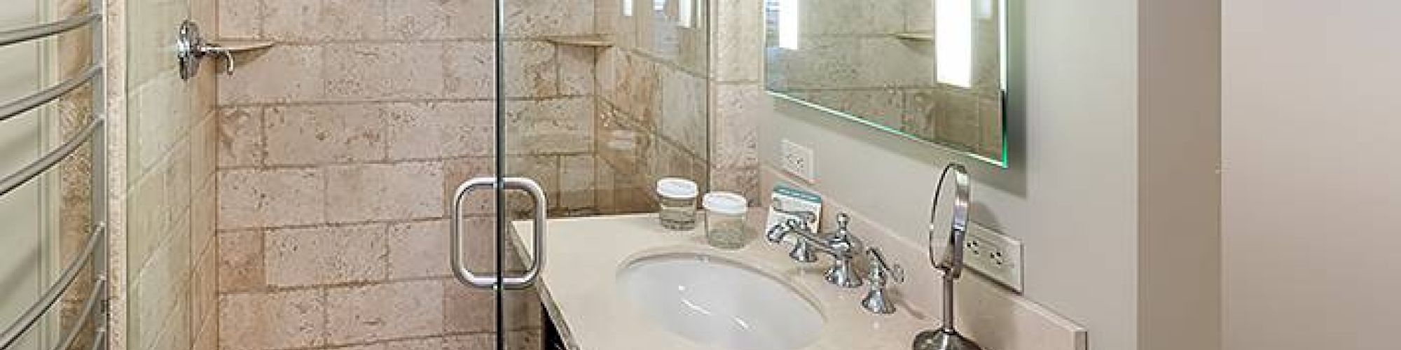 Modern bathroom with a glass shower, sink, mirror, and tiled walls.