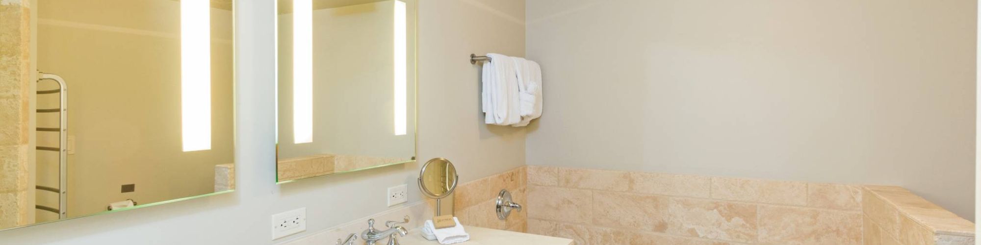 Modern bathroom with a tub, large mirror, sink, towels, and amenities.