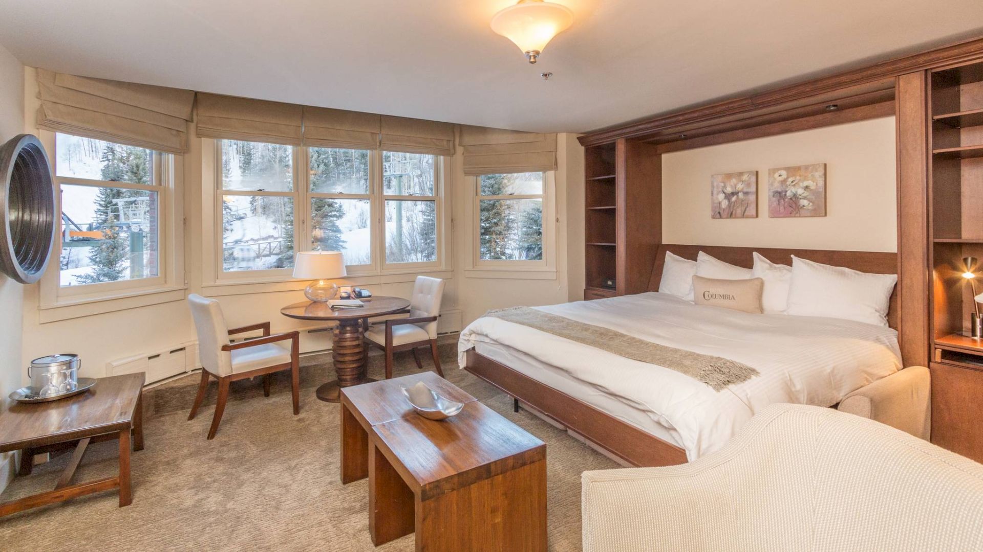A cozy bedroom with a bed, side tables, chairs, and a view through the window.
