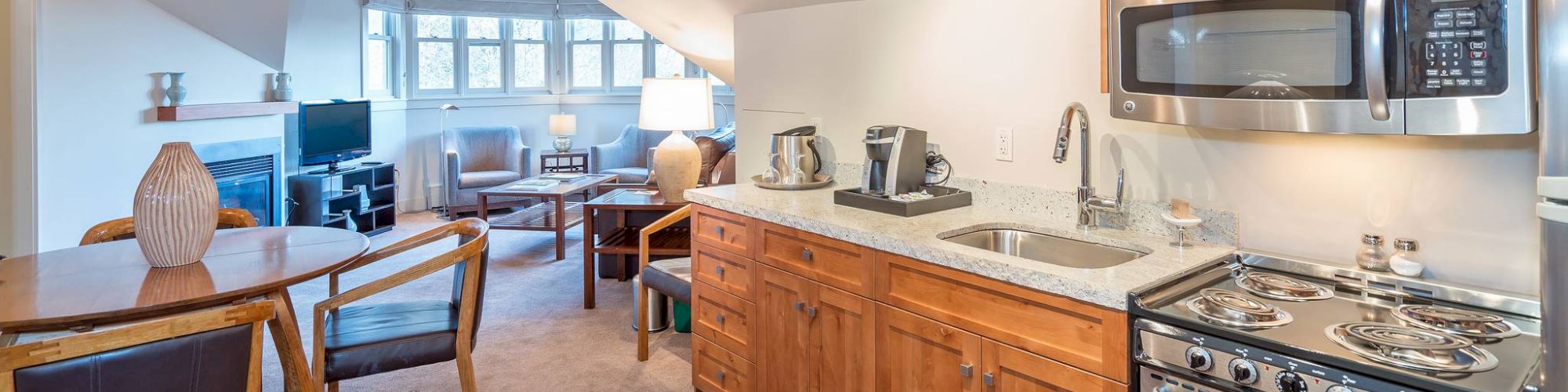 A modern kitchen with stainless appliances, wooden cabinets, and a dining area leading to a living room space.