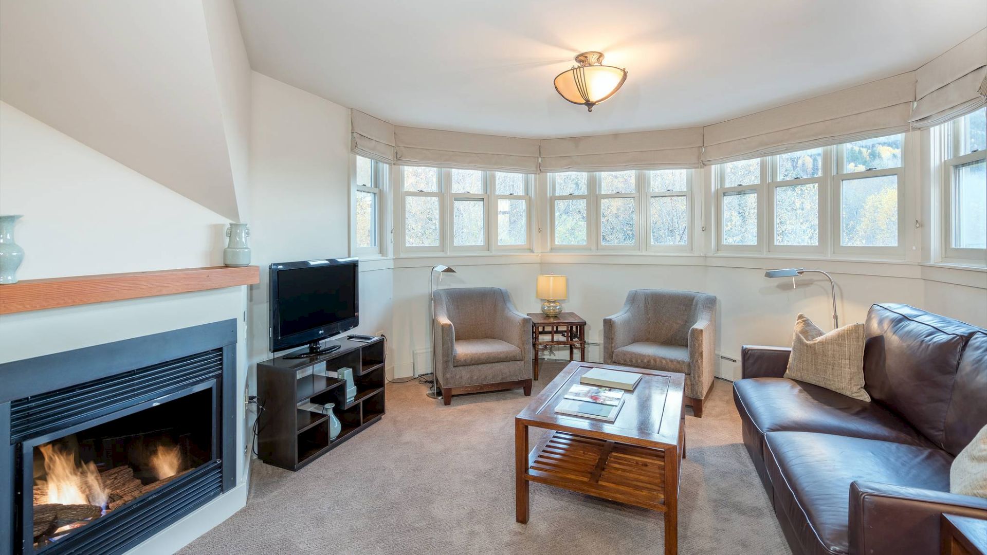 A cozy room with a fireplace, sofas, chairs, a TV, and large windows.