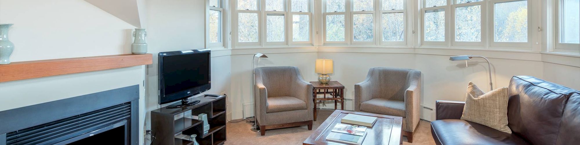 A cozy room with a fireplace, sofas, chairs, a TV, and large windows.