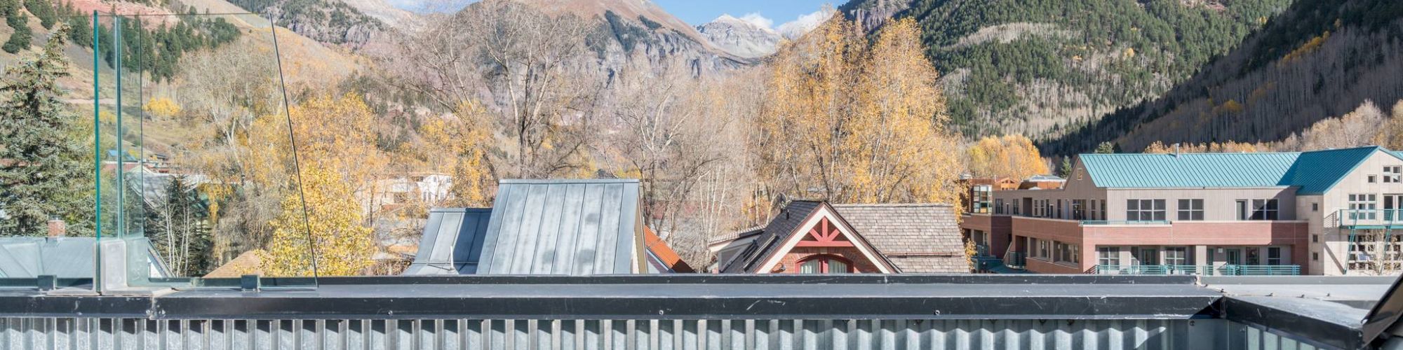 Balcony view of mountains, trees, and buildings with outdoor seating.