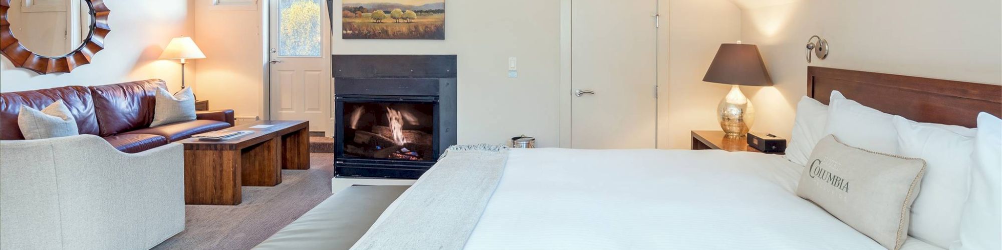 Cozy bedroom with a bed, fireplace, seating area, and warm lighting.