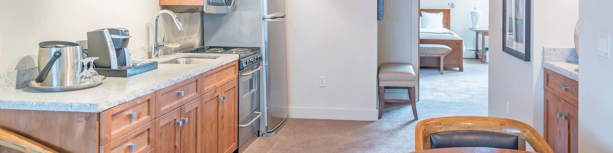 A cozy kitchen with wooden cabinets, steel appliances, a dining table, and an adjoining room view.