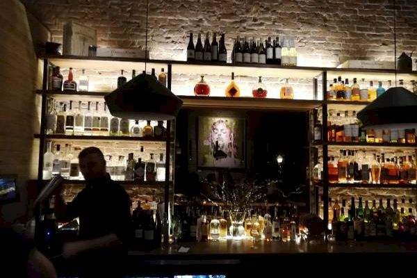 A dimly lit bar with bottles, a bartender at work, and stone wall decor.