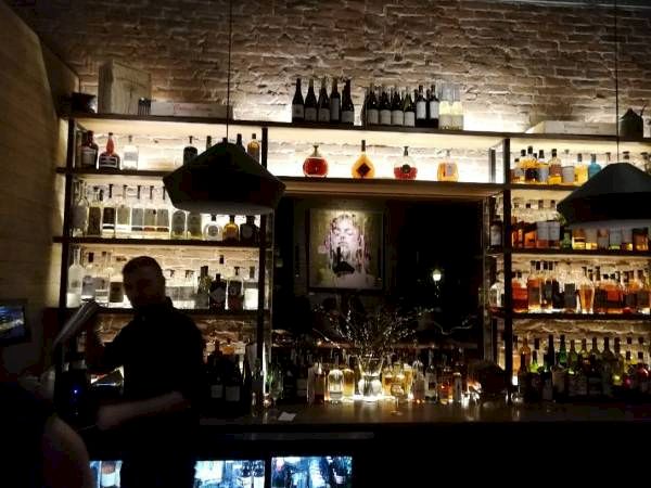 A dimly lit bar with bottles, a bartender at work, and stone wall decor.