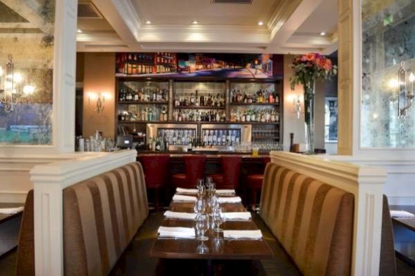 Elegant restaurant interior with tables set for dining and a well-stocked bar in the background.