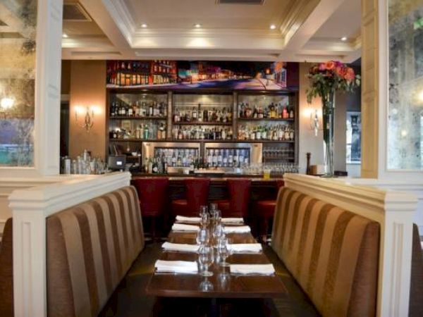 Elegant restaurant interior with tables set for dining and a well-stocked bar in the background.