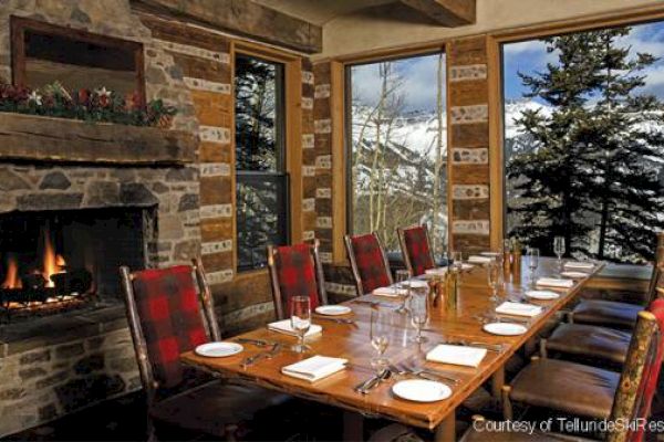 Cozy dining room with a long table set for a meal, a lit fireplace, and a mountain view outside.