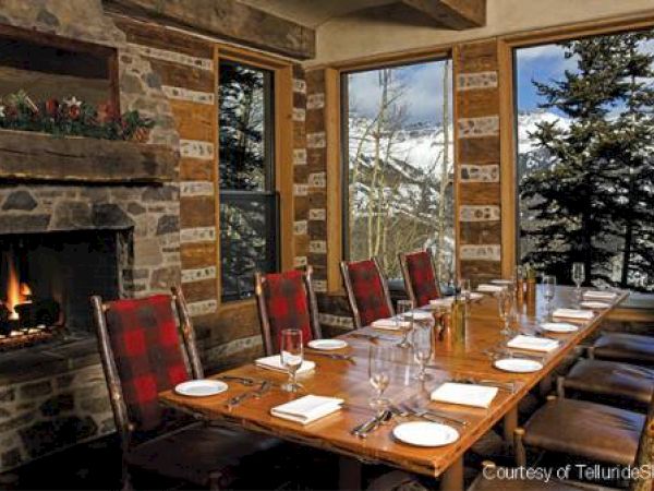 Cozy dining room with a long table set for a meal, a lit fireplace, and a mountain view outside.