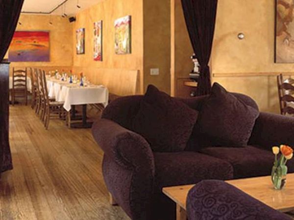A cozy interior with sofas, a small table with a flower, and a dining area in the back.
