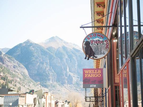 Storefronts with signs, "Brown Dog Pizza" and "Wells Fargo ATM," and mountains in the background.