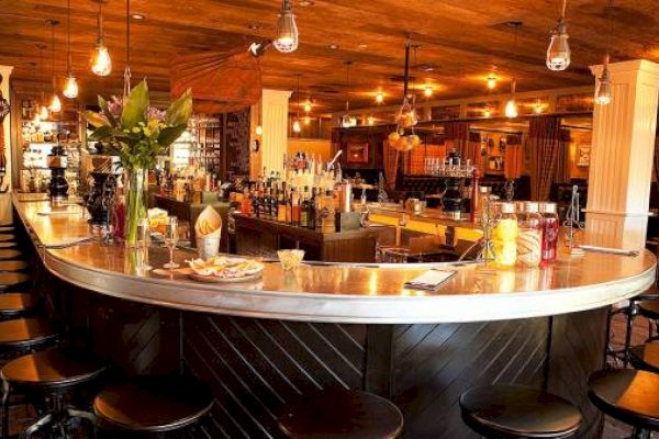 A cozy bar with stools, pendant lights, and shelves with bottles.