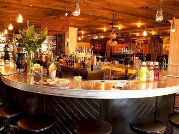 A cozy bar with stools, pendant lights, and shelves with bottles.