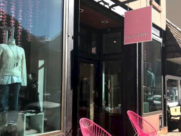 Boutique store front with mannequin, pink signage, and chairs.